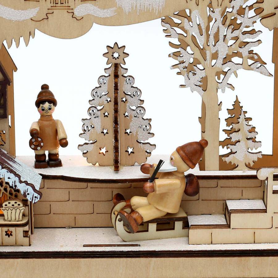 Winterfigur mit mütze und weissen Bart auf einem Schlitten und Winterkind mit Lebkuchen in der Hand mit verschneitem Weihnachtsbaum