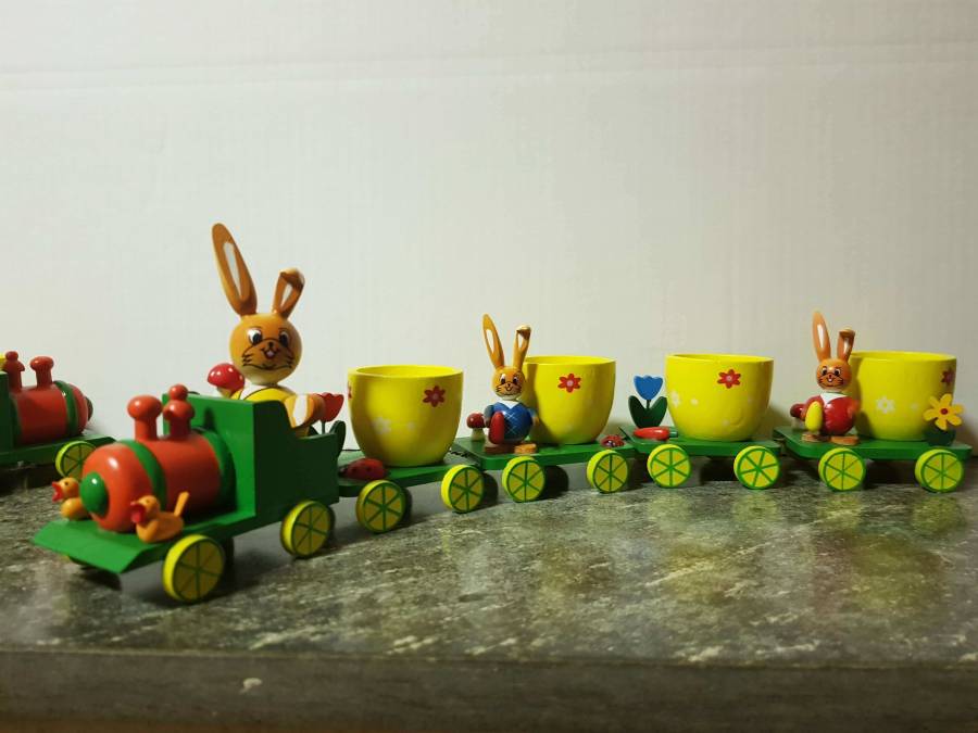 grüner Holzzug mit vier gelben Eierbechern verteilt auf vier Anhänger.